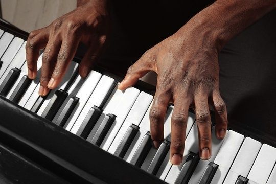 Dark-skinned hands playing a piano keyboard in close-up