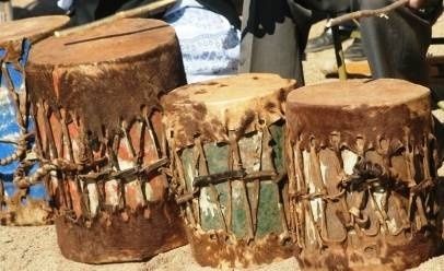 Three weathered rope-tensioned African drums displayed outdoors